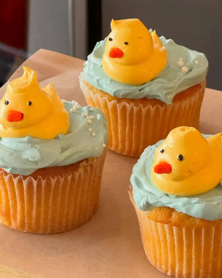 Vanilla cupcakes topped with blue frosting and yellow ducks made of frosting
