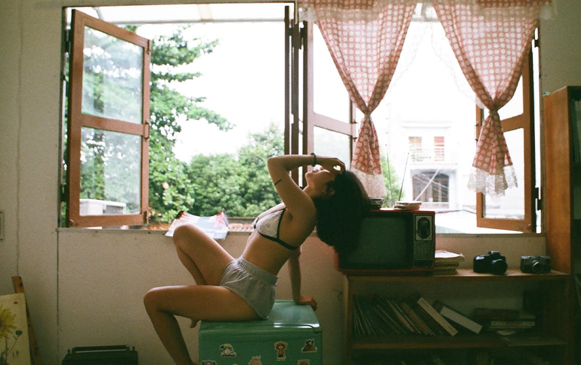 a woman dressed in shorts and a bra sits by a window