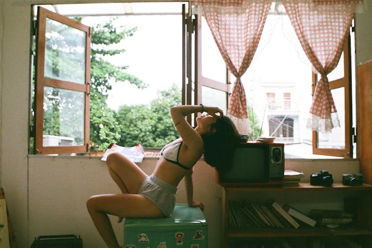 a woman dressed in shorts and a bra sits by a window