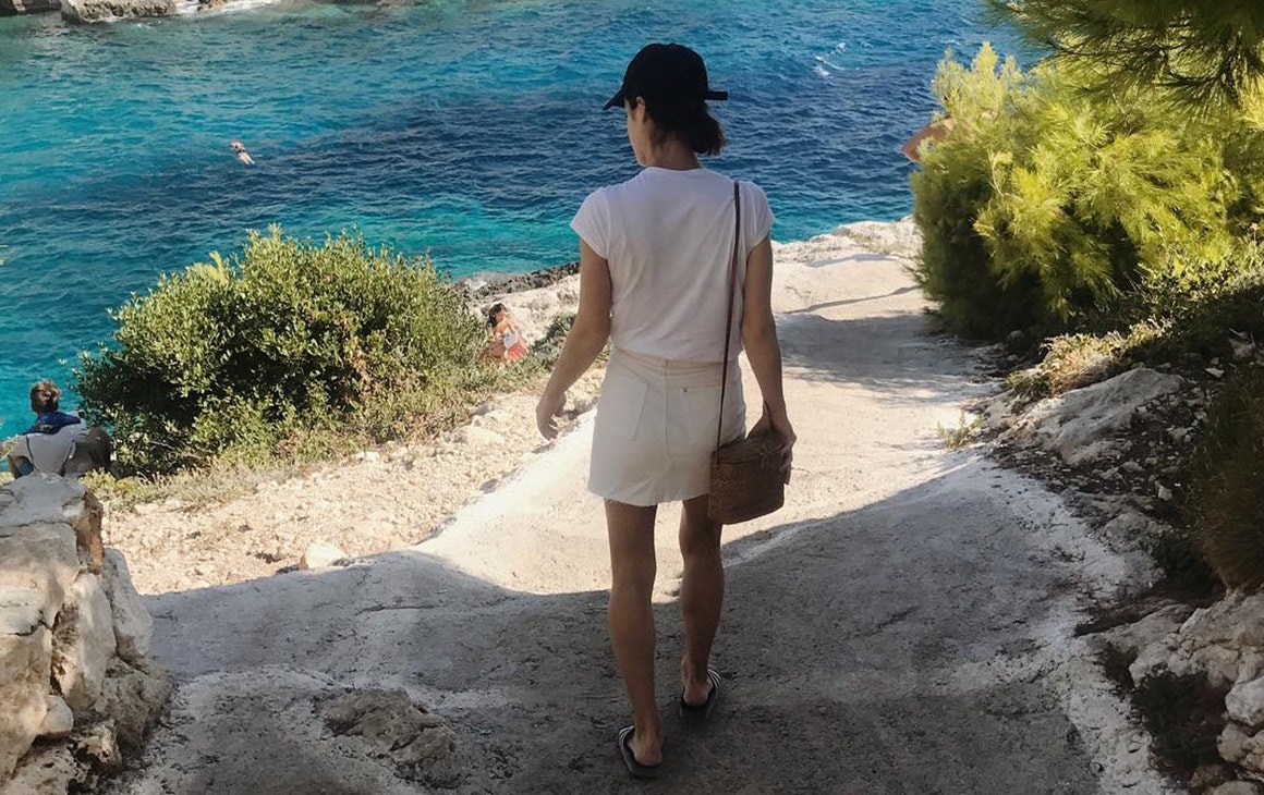 a person wearing a cap, walks towards the water.