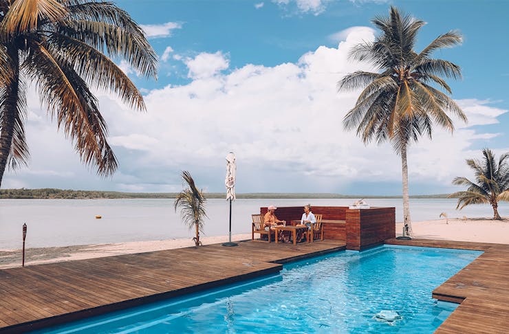 a couple relax by the pool at Tiwi Island Retreat, surrounded by white sand and palm trees
