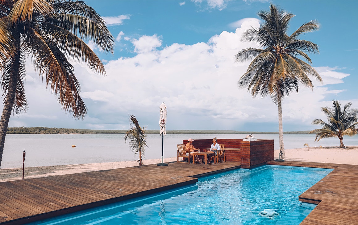 a couple relax by the pool at Tiwi Island Retreat, surrounded by white sand and palm trees
