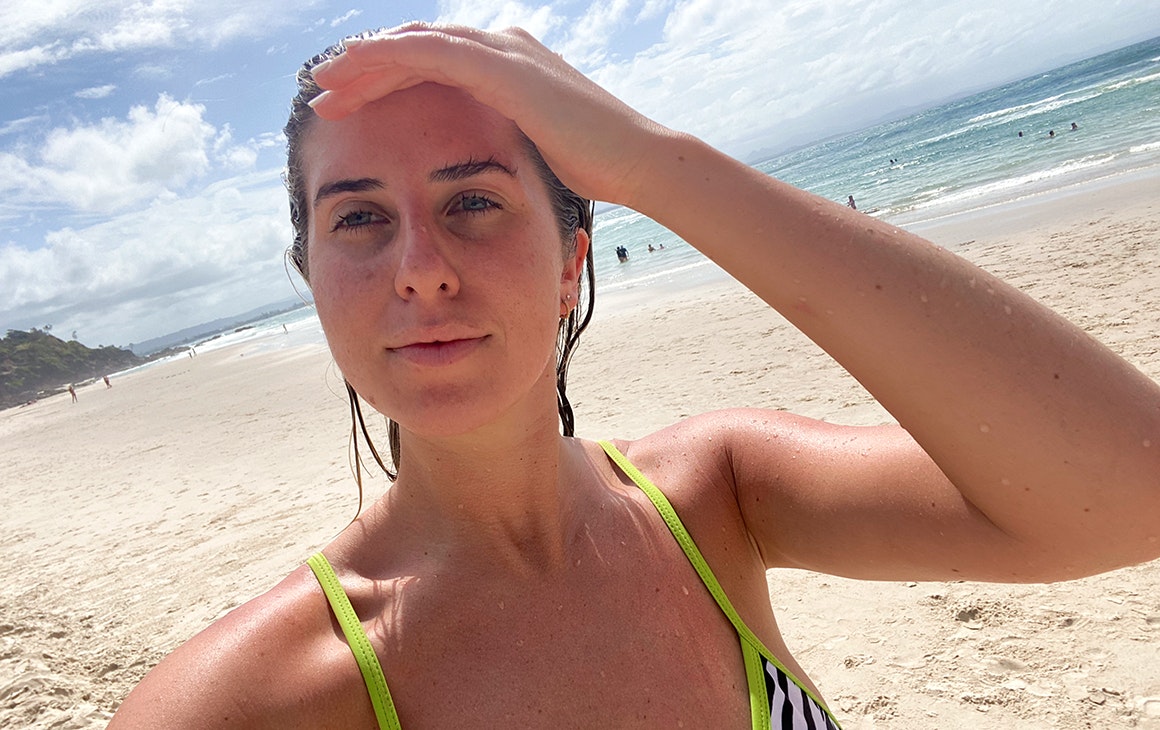 a woman at the beach, shading her eyes from the sun with her hand.