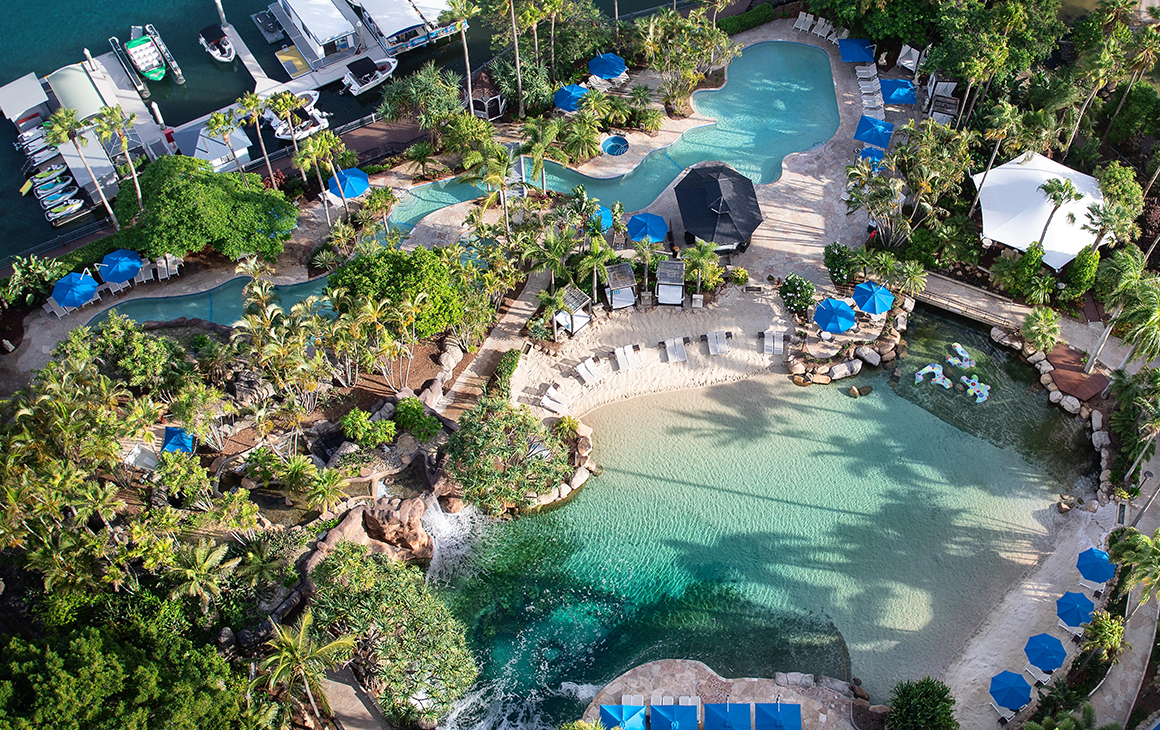 a bird's eye view of two sparkling pools fringed by palm trees.