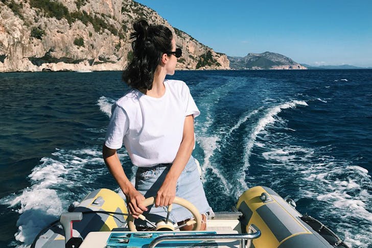 a young woman wearing a white t-shirt looks over her shoulder while driving a boat.
