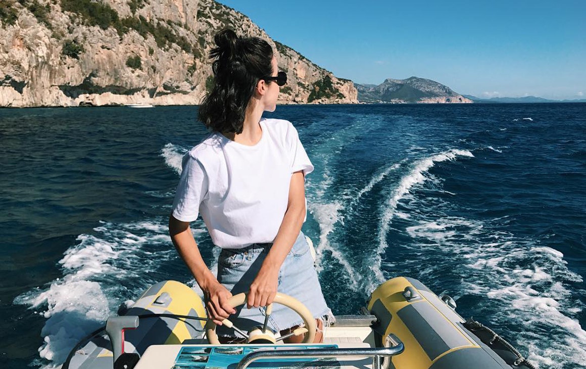 a young woman wearing a white t-shirt looks over her shoulder while driving a boat.