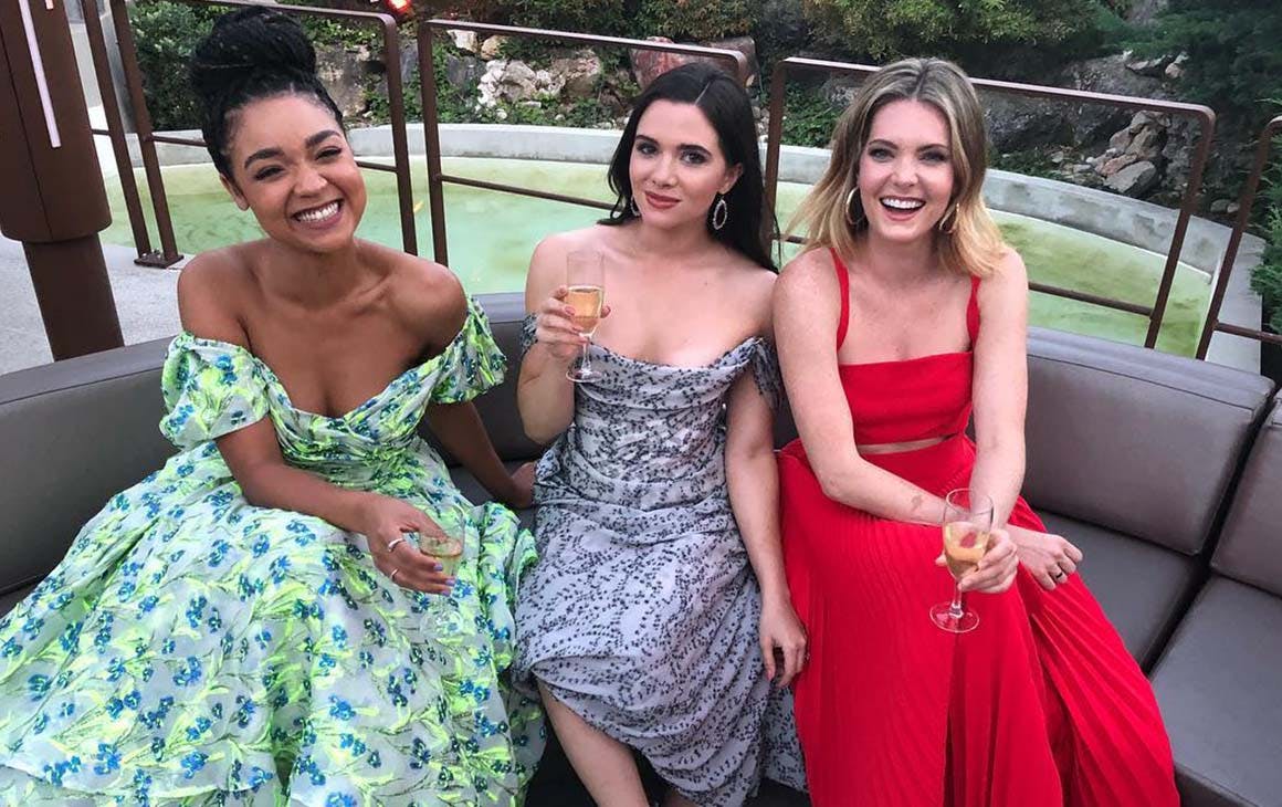 Aisha Dee, Katie Stevens and Meghann Fahy of The Bold Type pose on a couch together in stunning dresses. 