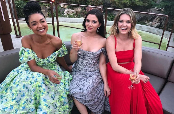 Aisha Dee, Katie Stevens and Meghann Fahy of The Bold Type pose on a couch together in stunning dresses. 