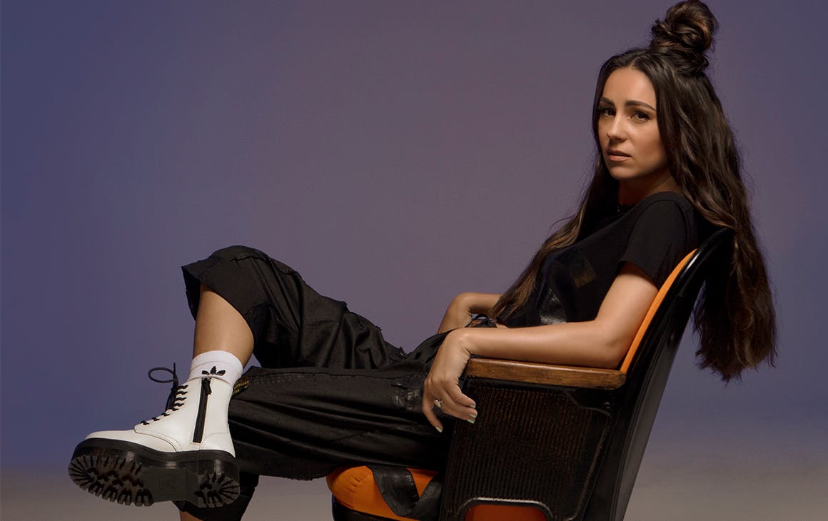 Amy Shark leans back in a chair with her legs crossed.