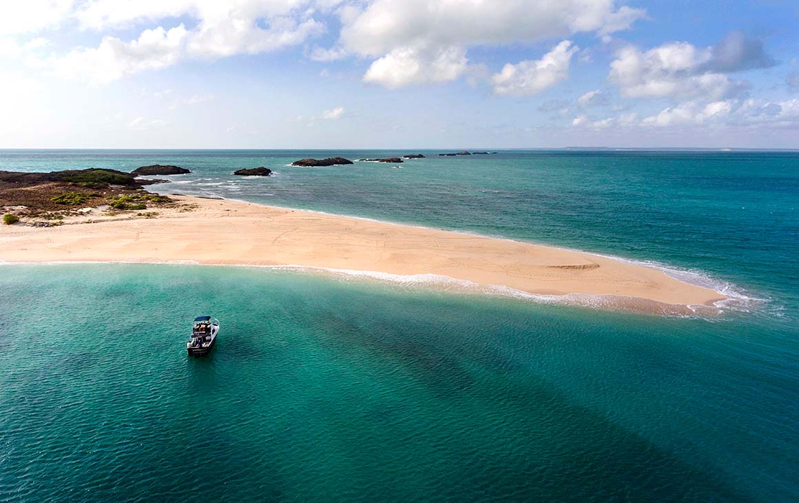 the stunning blue waters of Arnhem Land meets golden sand. A boat floats nearby.