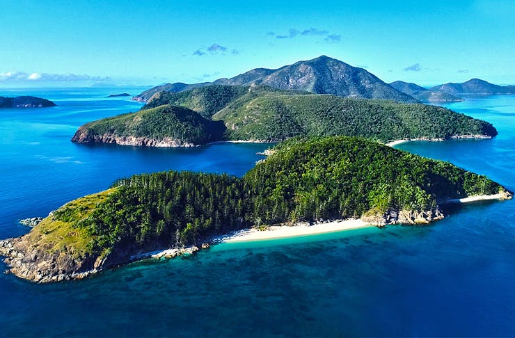Shaw Island in the Whitsundays is surrounded by deep, navy blue water and is covered in lush, green rainforest.