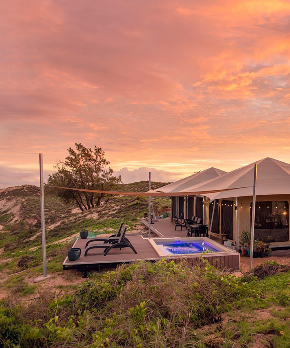 a stunning pink sky lights up over the sea with glamping tents dotted along the sand.