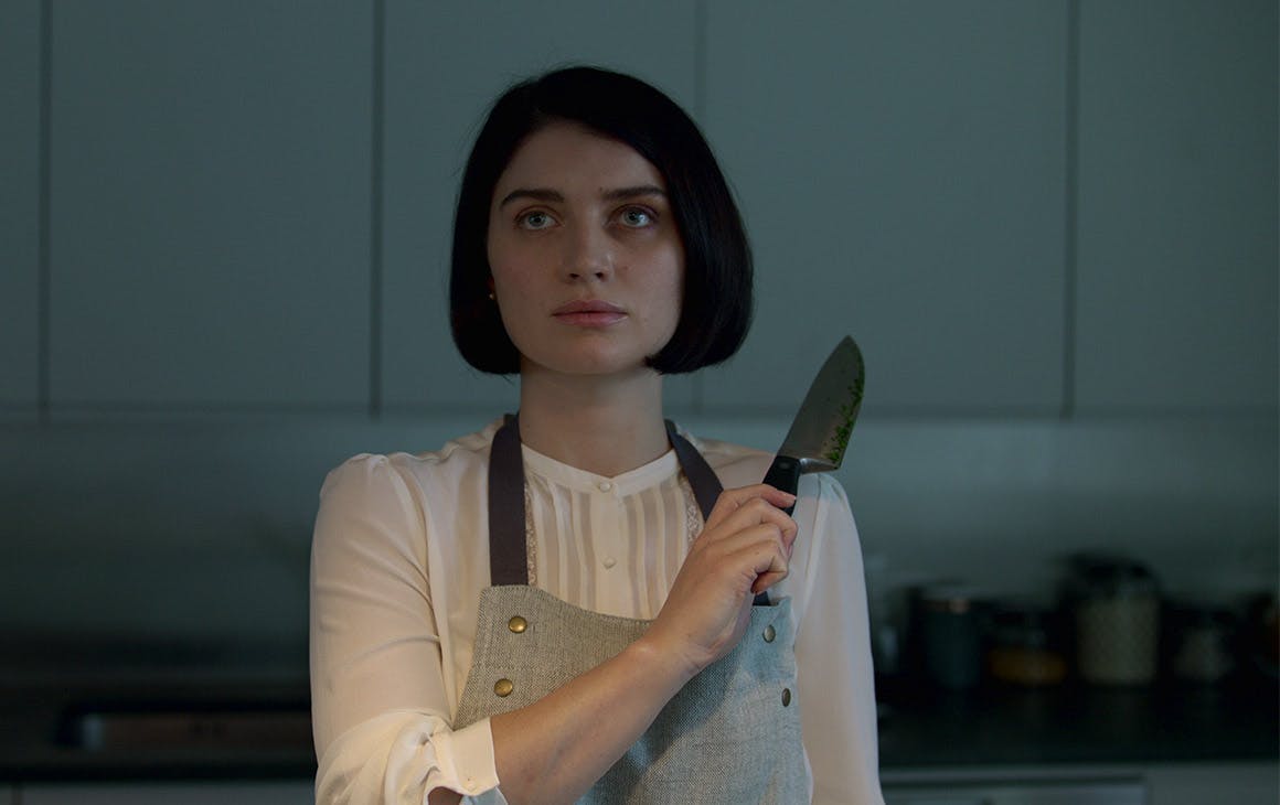 a woman holds up a knife, while standing in the kitchen.