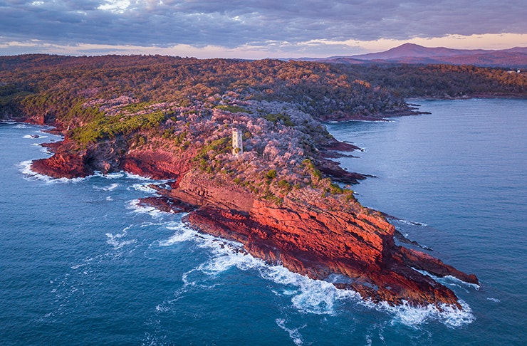 aerial sunrise view of pointed clifftop with tower on top of it
