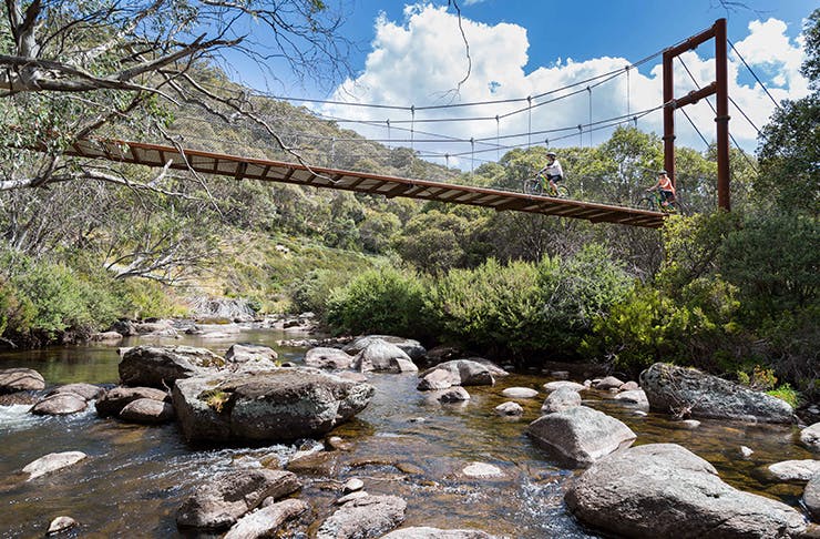 two riding bikes across suspension  bridge over river