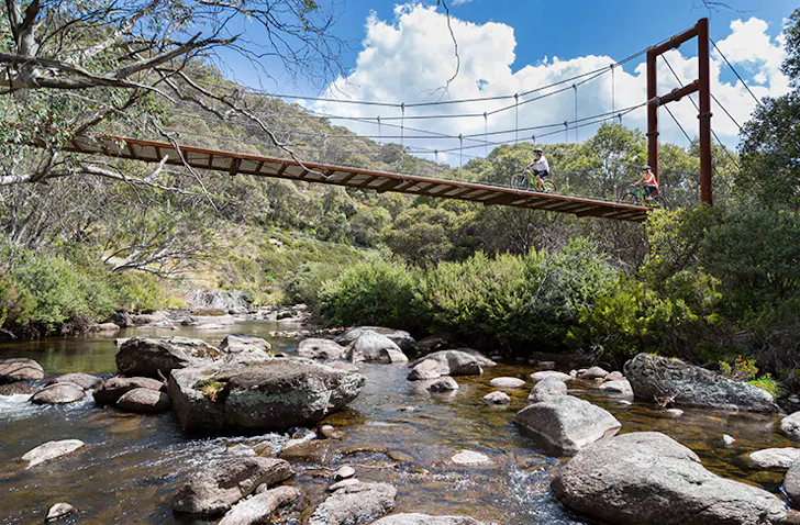two riding bikes across suspension  bridge over river