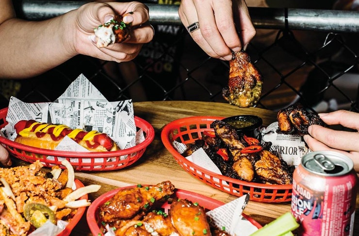 hands reaching over chicken wings, hot dogs and beer