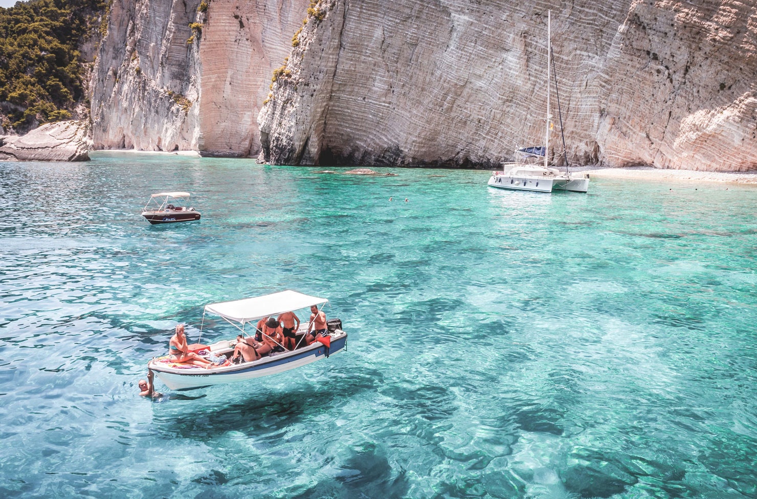 a boat floating near a white cliff in bright blue water