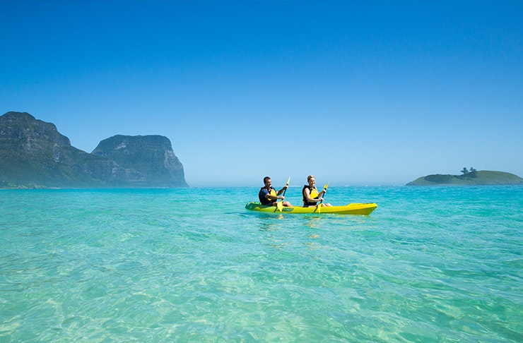 two people kayaking on clear waters with mountain behind