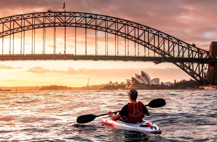 person kayaking at sunrise in sydney harbour before the harbour bridge