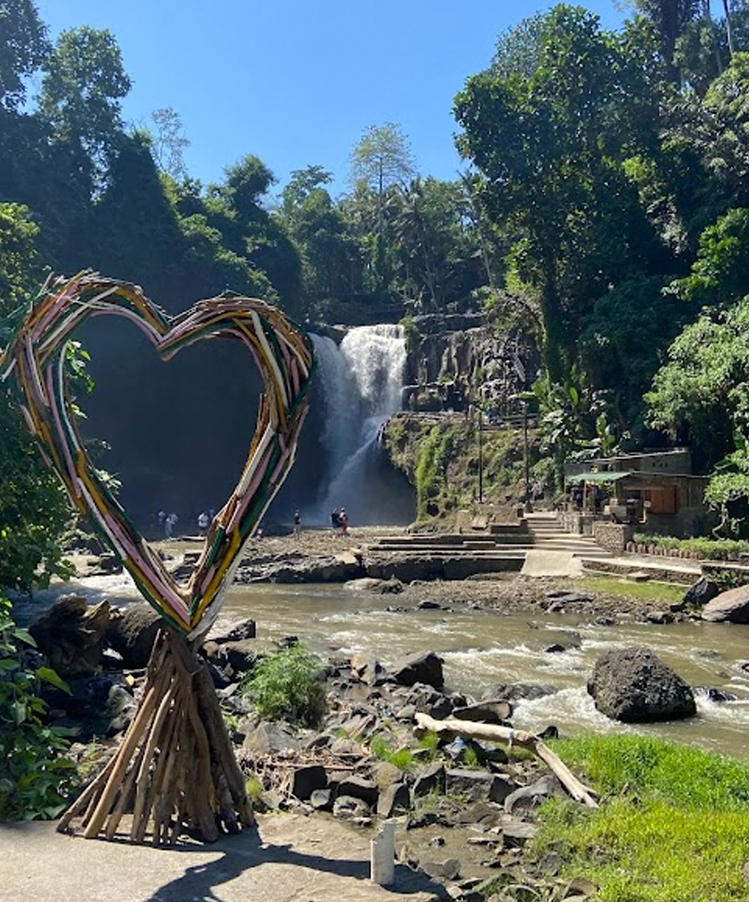 people walking around a waterfall on a sunny day