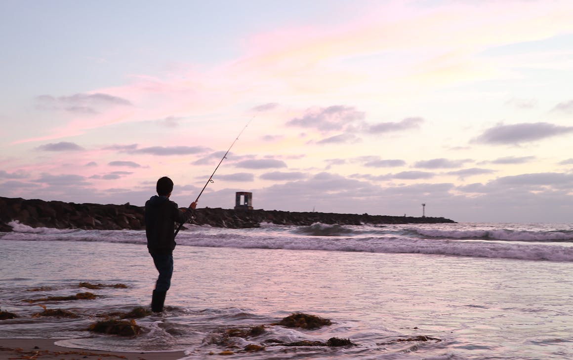 Silhouette of a person fishing while ankle deep in the water