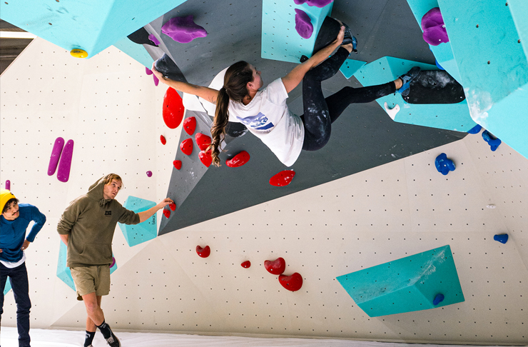 girl climbing bouldering wall with two friends cheering on the groudn