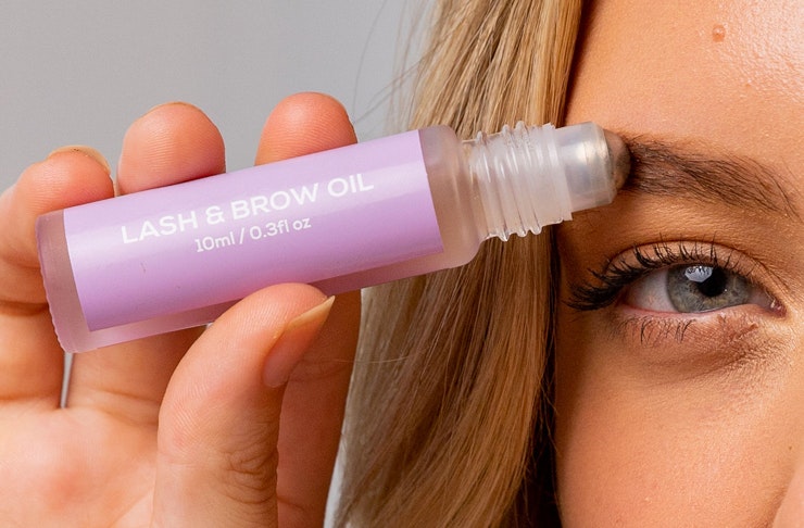 person holding brown and lash oil vial up to their eyebrow