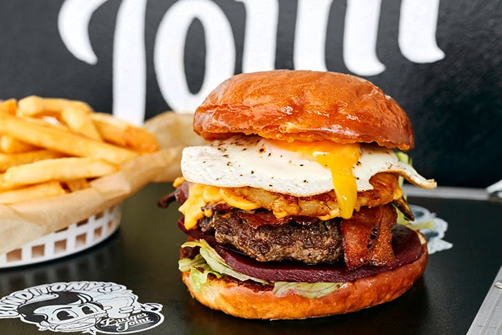 big burger overflowing with fried egg on table next to bowl of fries