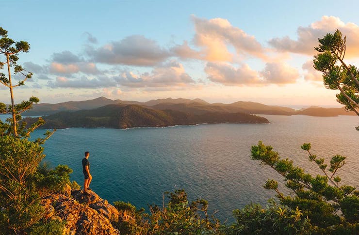 a man stands on a cliff looking out a cluster of stunning islands 