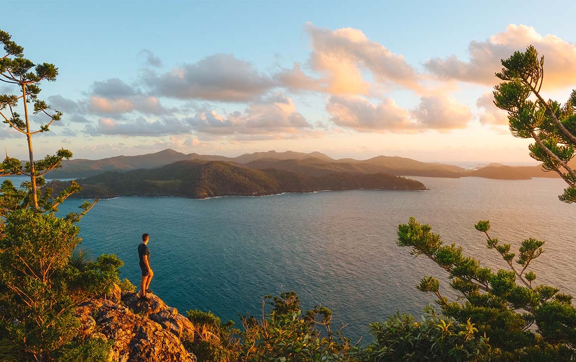 a man stands on a cliff looking out a cluster of stunning islands 