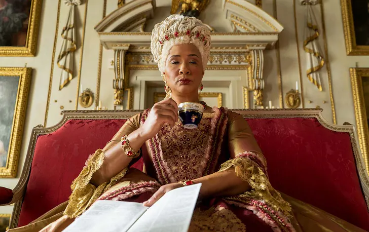 Queen Charlotte of Bridgerton holds a paper and sips a cup of tea.