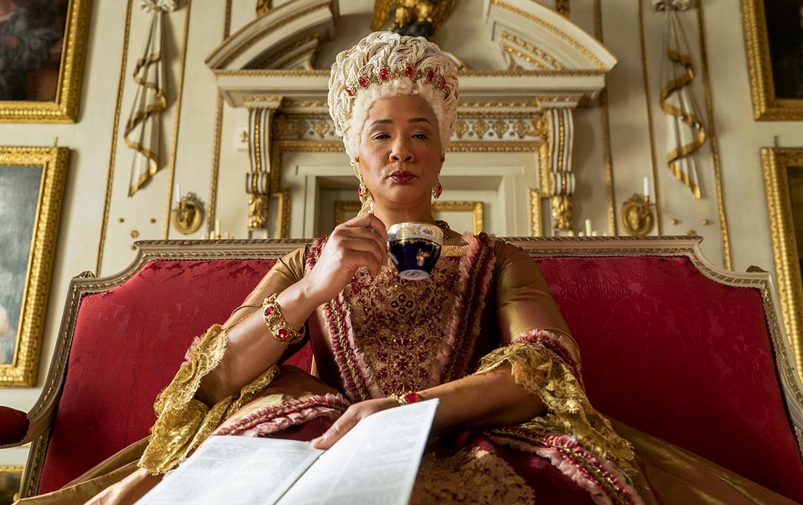 Queen Charlotte of Bridgerton holds a paper and sips a cup of tea.