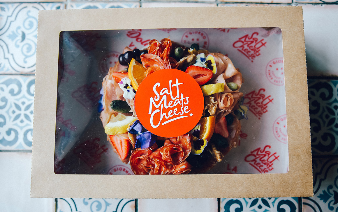 a wheel of cheese with flowers and fruit on top in a box