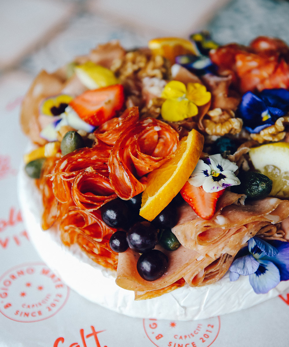 a wheel of cheese with flowers and fruit on top
