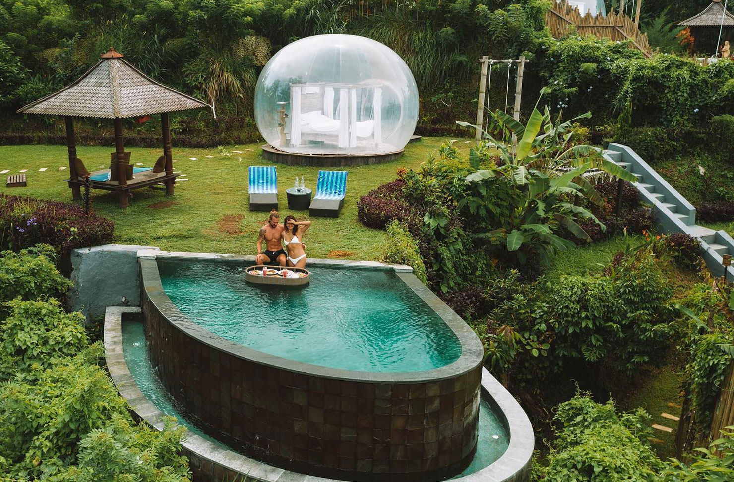 two people sitting in a pool at a bubble hotel in the jungle