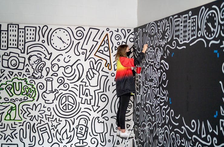 girl standing on ladder painting wall