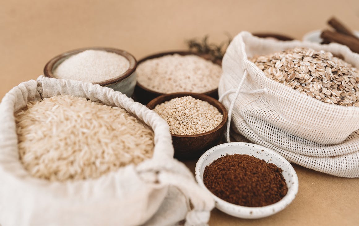 Hessian bags are filled with rice and rolled oats. Around it are small ceramic bowls filled with sugar and powder.