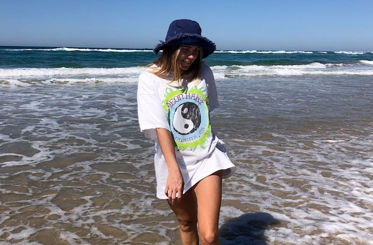 girl wearing tshirt and bucket hat standing on shoreline of beach on a sunny day