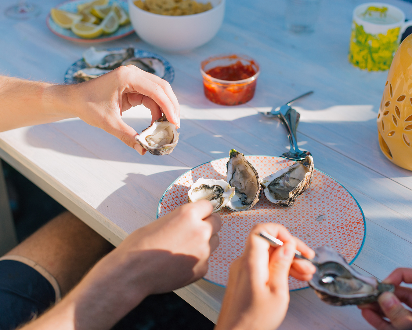 hands reaching for and holding oysters and a summery table spread
