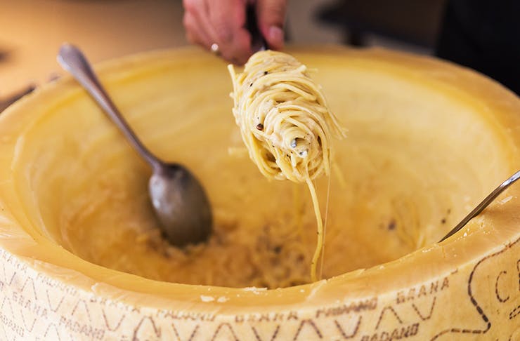cacio e pepe pasta dipped into giant, creamy cheese wheel