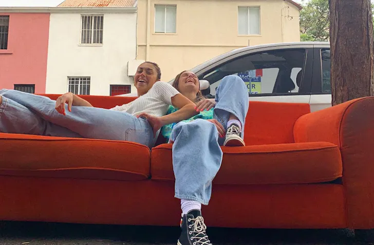 two girls sitting on a couch outdoors, both are laughing