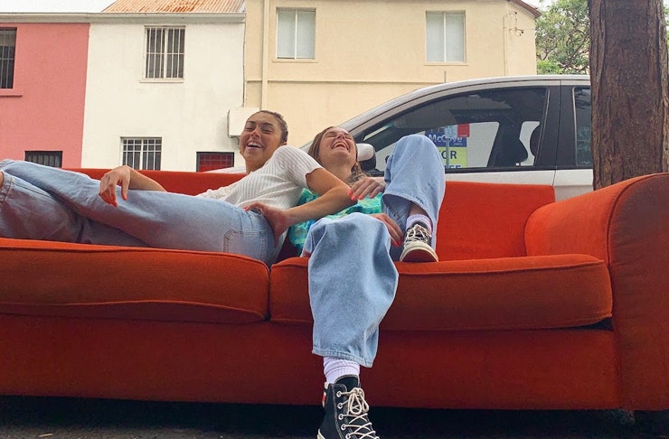 two girls sitting on a couch outdoors, both are laughing