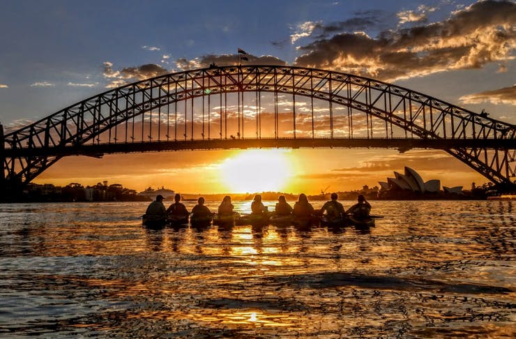 several kayakers lined up in front of sydney harbour bridge at sunrise