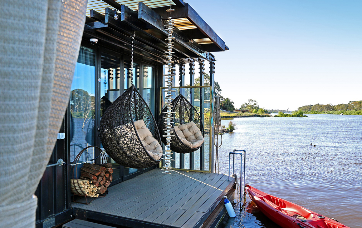Two hanging chairs on a deck on the river.