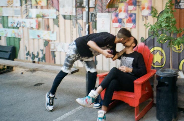 one person sitting down on a chair, another person is standing and leaning over to kiss them