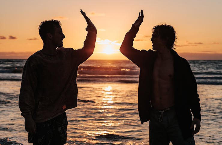 two men high five on the beach at sunset