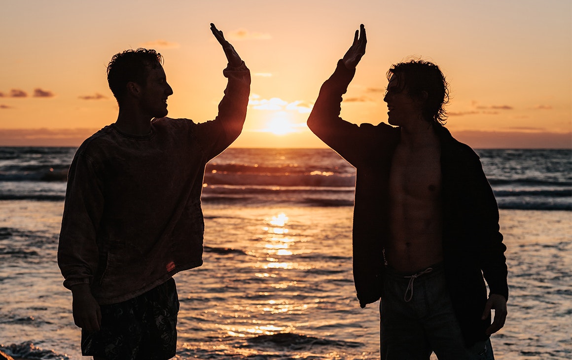 two men high five on the beach at sunset