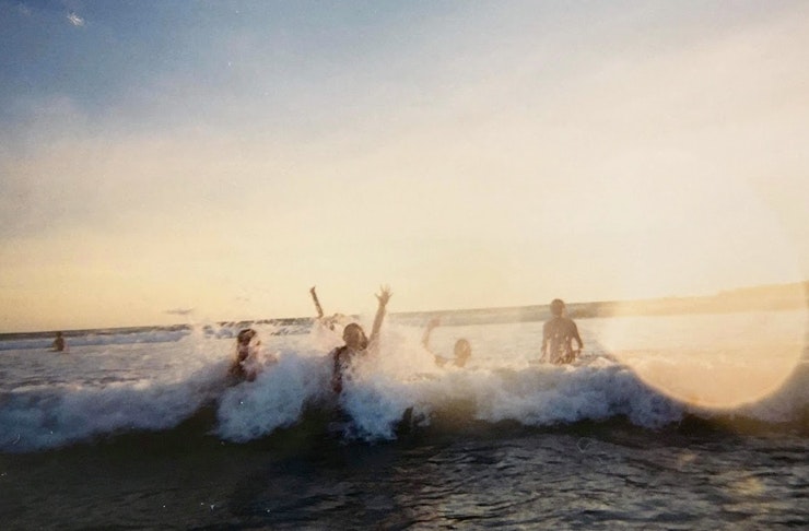 people splashing in waves at a beach at sunsey
