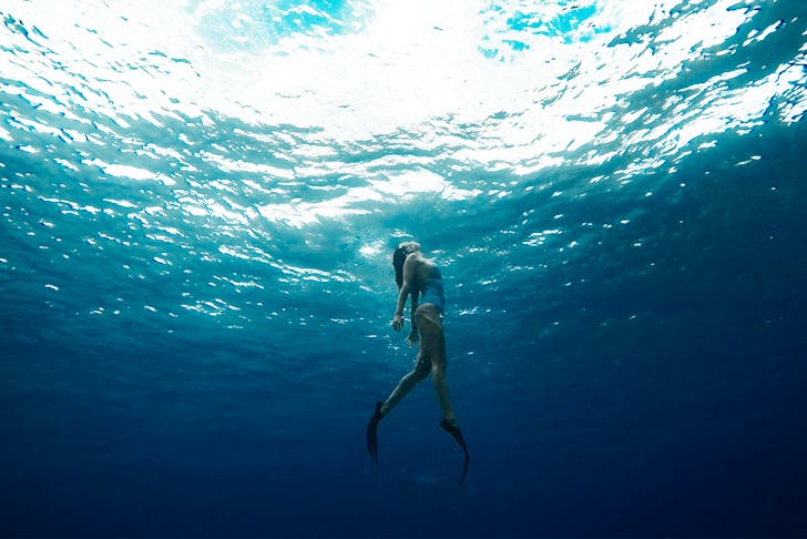 a woman swims towards the surface of the ocean.
